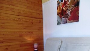 A room with a wooden wall, a white sofa, a small wooden table with a remote control, and a lamp on a side table. - Les Genêts - Brocas - Gîte (BROCAS)
