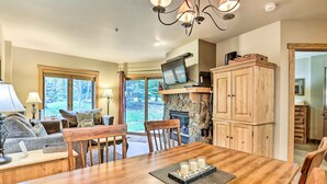 A dining area with a wooden table, chairs, and a fireplace. There is a television on a wooden shelf above the fireplace. - Cozy Red Hawk Lodge Condo: Walk to River Run! (Keystone)