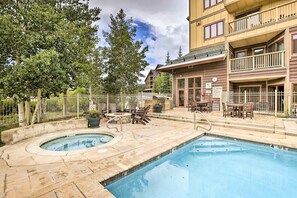 A pool area with hot tub and lounge chairs, surrounded by a fence and trees.