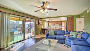 A living room with a blue sofa, a glass coffee table, and a ceiling fan. - 'breeze By the Pool' Chula Vista Home w/ Game Room (Chula Vista)
