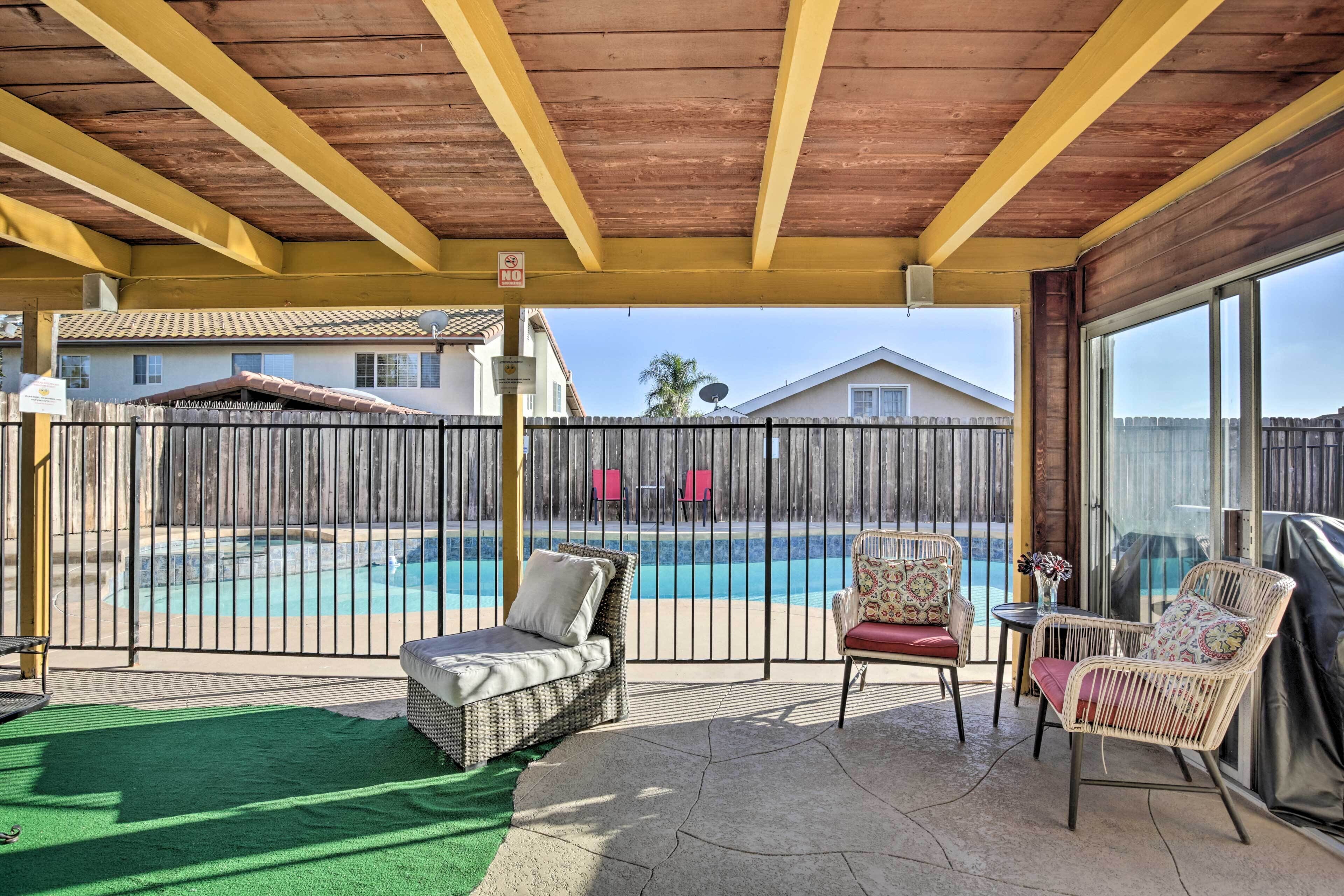 A covered patio area with outdoor furniture, a pool, and a view of neighboring houses.
