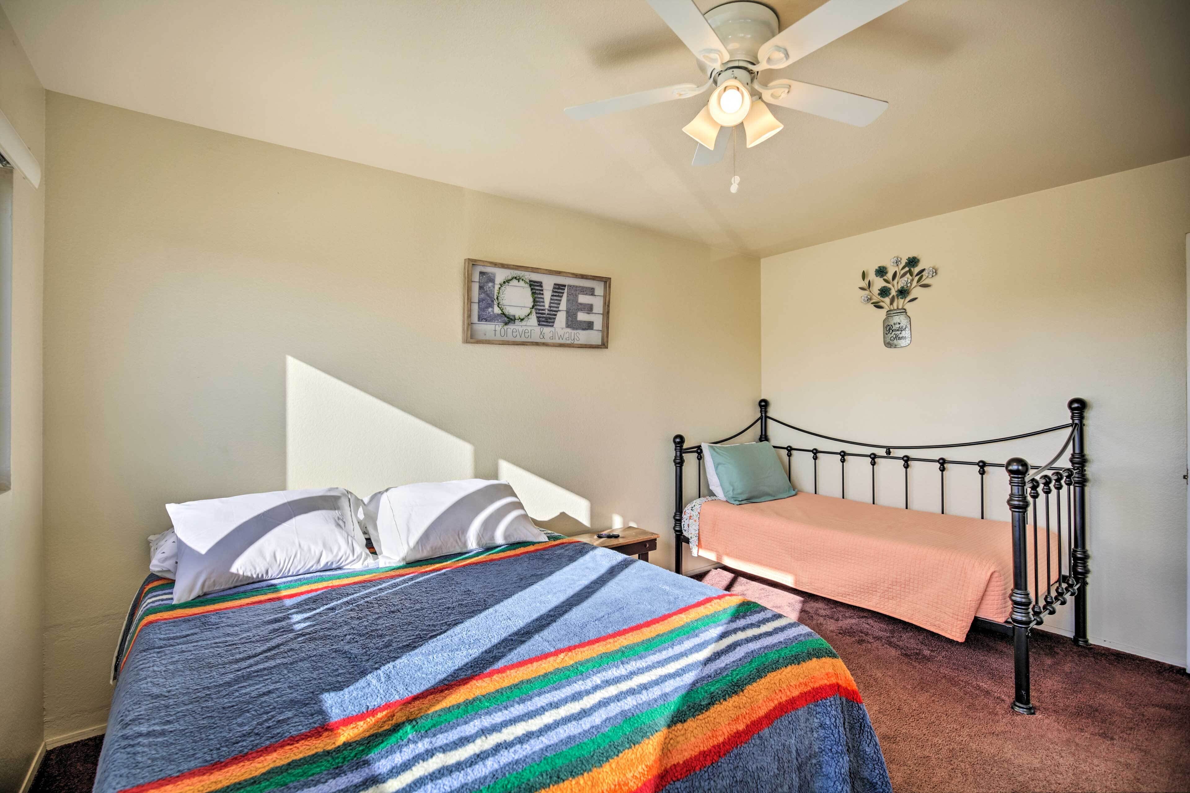 Een slaapkamer met een bed, nachtkastje, plafondventilator, muur met een 'LOVE' bord en een kleine wanddecoratie.