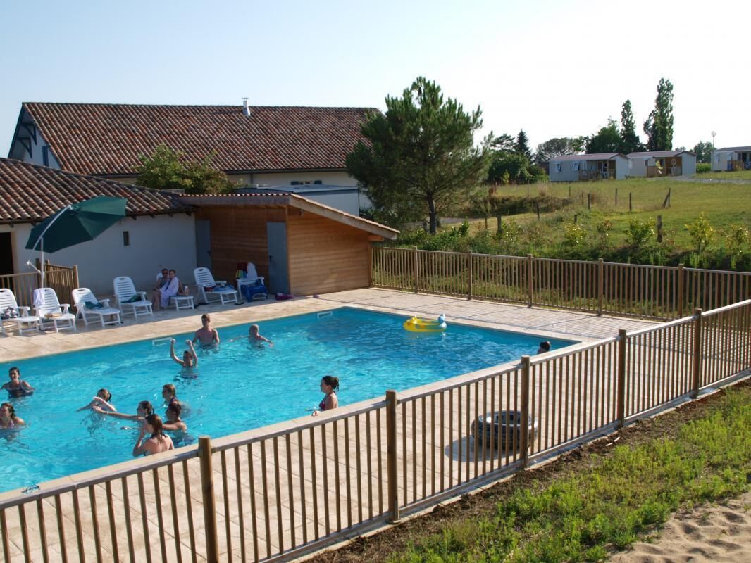 A swimming pool with people, a fenced area, and a building with a tiled roof.
