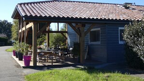 A covered outdoor seating area with tables and chairs, connected to a building with a tiled roof.