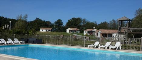 A swimming pool with white lounge chairs and a wooden play structure.