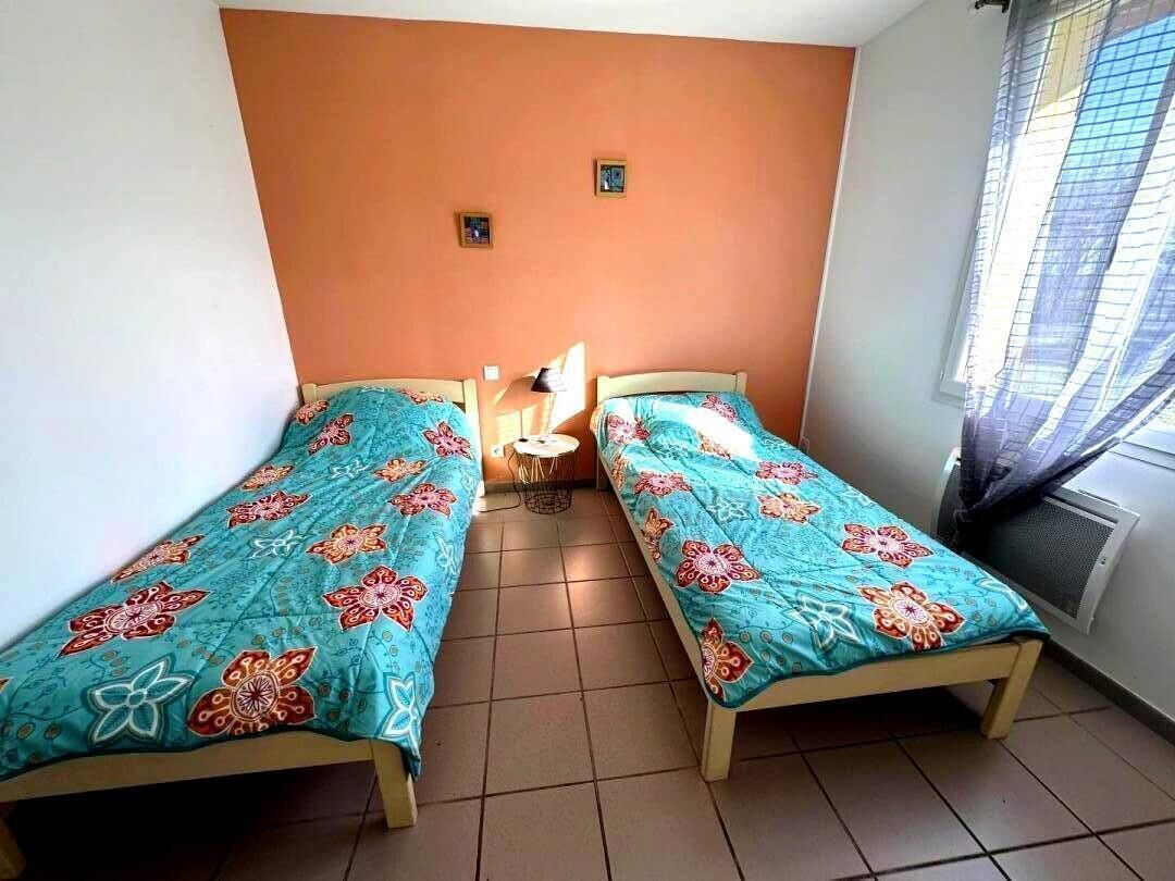 Een kamer met twee eenpersoonsbedden, een klein rond tafeltje en een raam met jaloezieën.