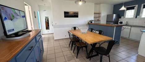 Uma cozinha moderna com mesa de jantar de madeira, cadeiras pretas e uma TV no balcão.