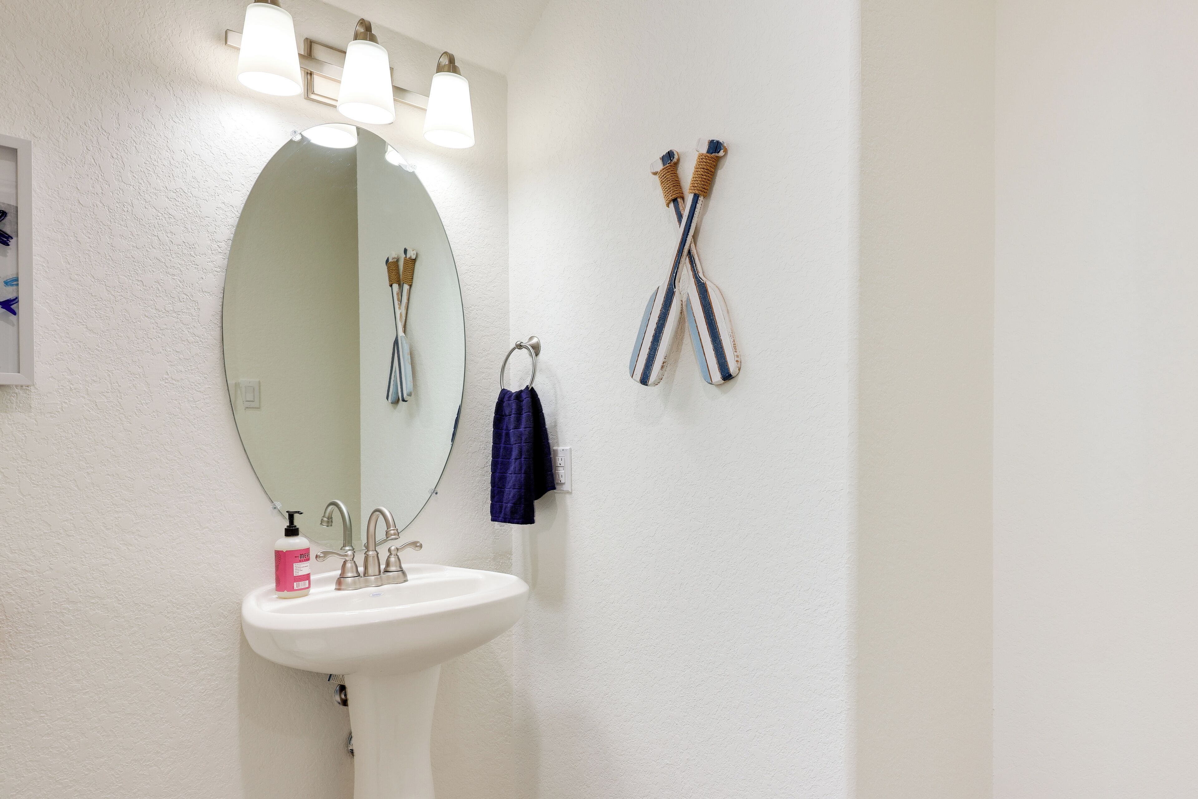 A bathroom with a white sink, a round mirror, and two toothbrushes hanging on the wall.