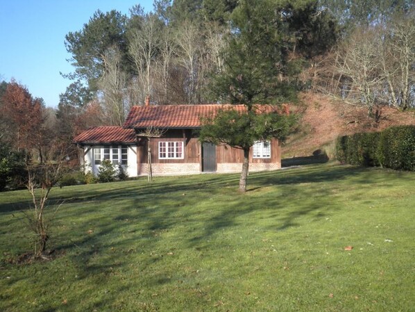A wooden house with a red roof, surrounded by a well-maintained lawn and trees.