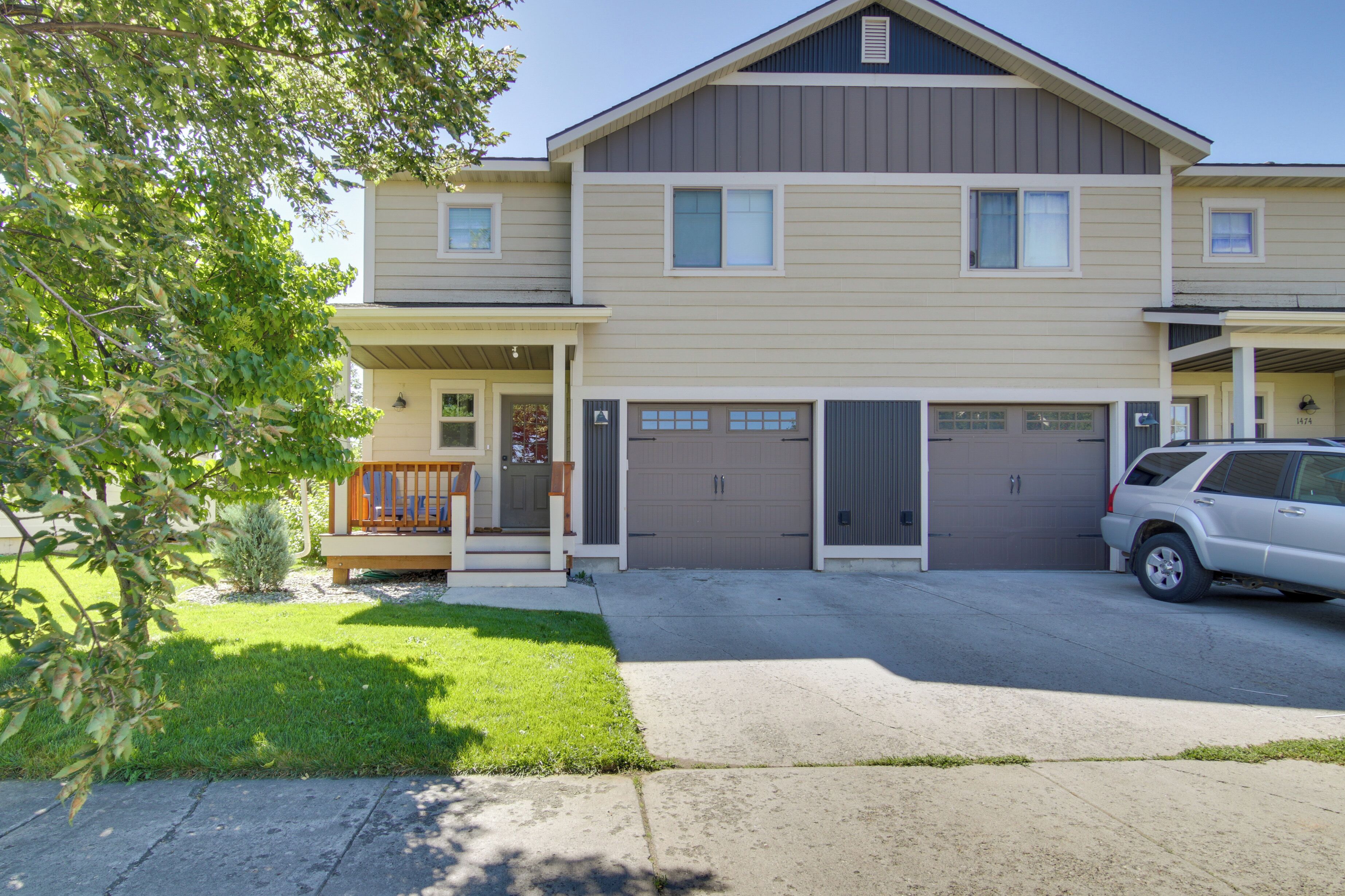 A two-story residential building with a front porch, a garage, and a driveway.