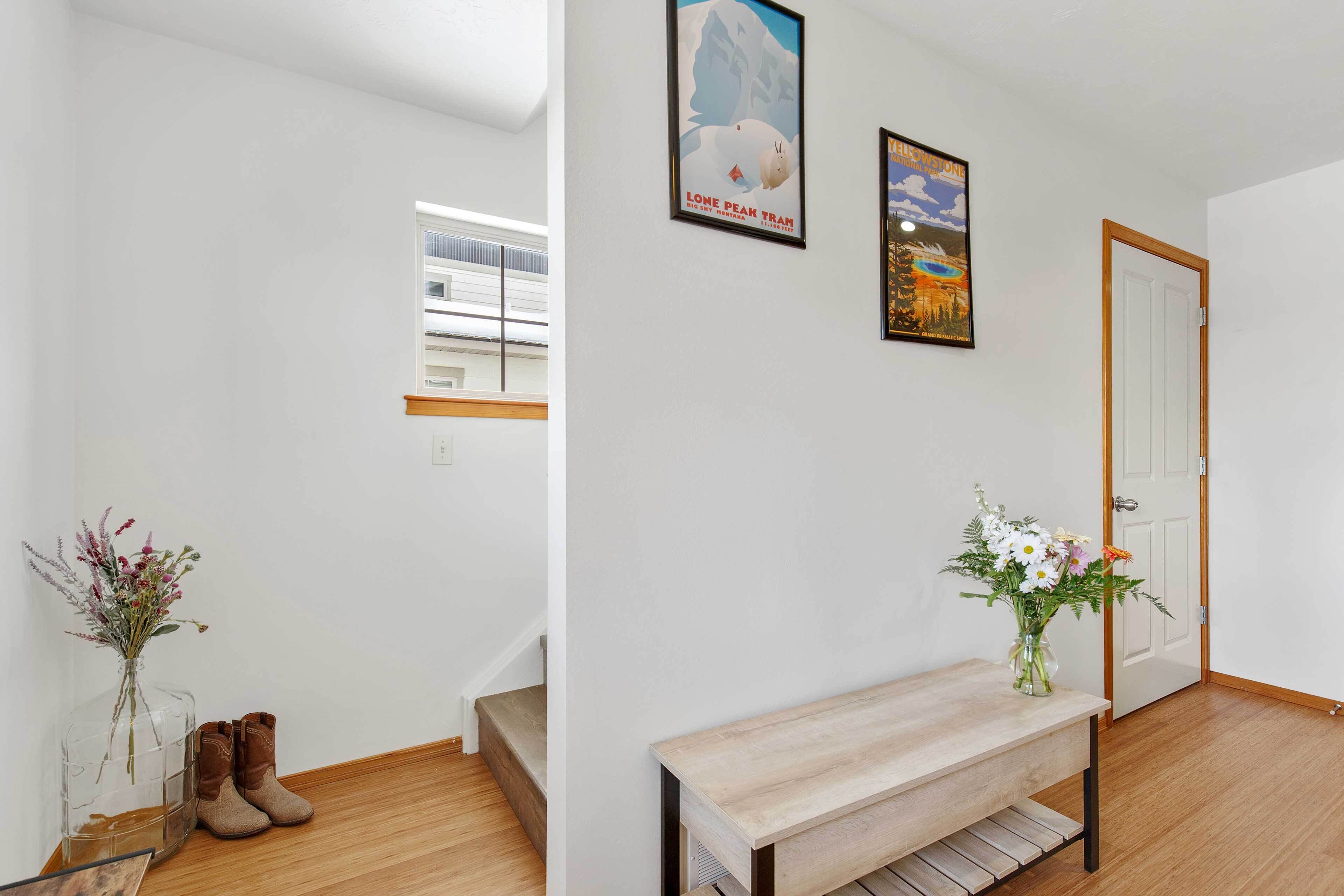 Un couloir avec un banc en bois, un vase de fleurs, une paire de bottes et deux tableaux encadrés accrochés au mur.