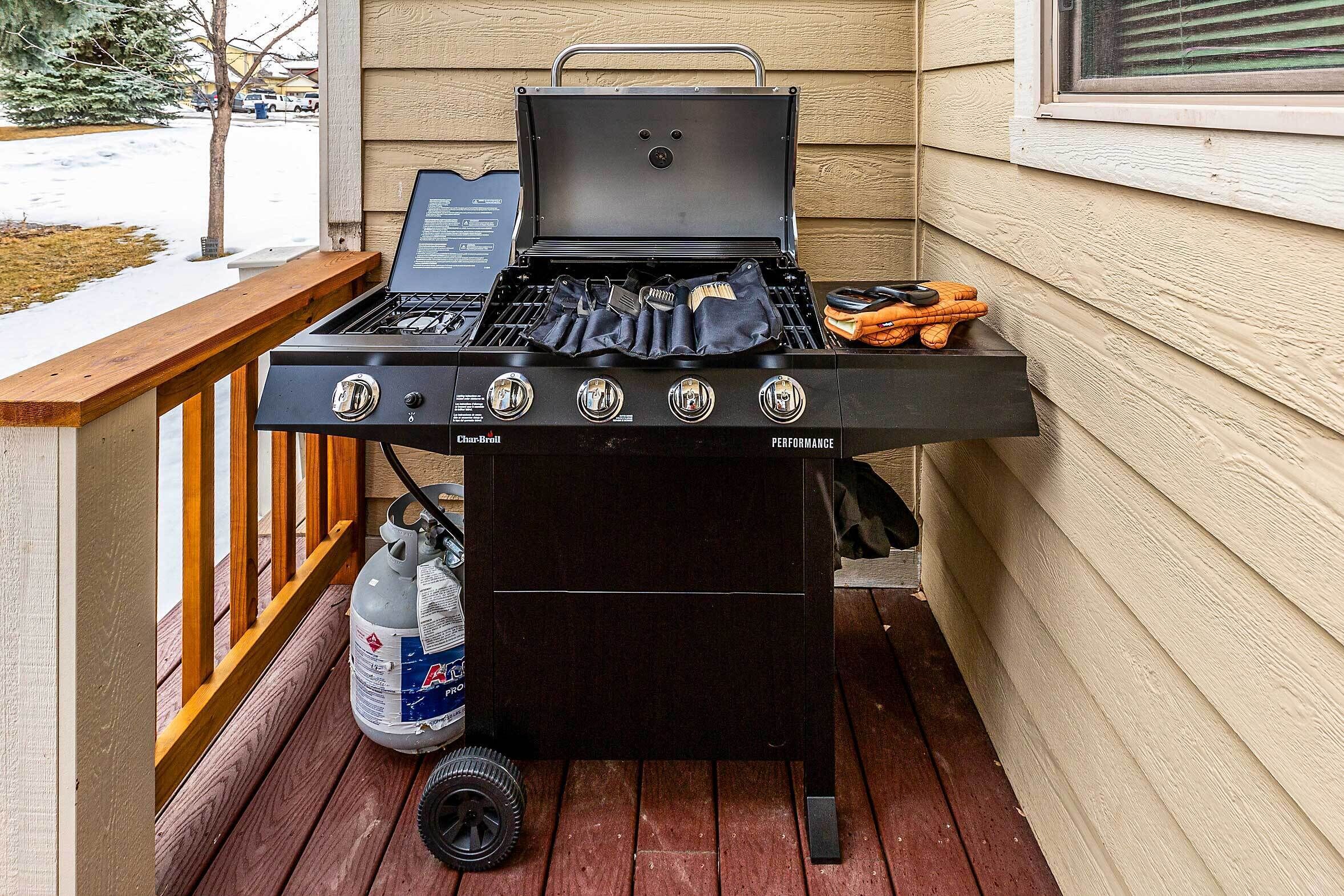 A Char-Broil Performance grill with a side table, a propane tank, and grilling tools on a wooden deck.