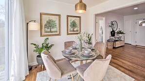 Un coin repas avec une table ronde dressée pour quatre personnes, entourée de chaises rembourrées, un vase rempli de fleurs et des tableaux encadrés accrochés au mur.