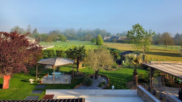 Un jardin agrémenté d’une pergola, d’un espace détente et offrant une vue sur un champ verdoyant.
