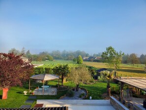 A garden with a pergola, seating area, and a view of a green field. - Prune - St-vincent-de-paul (ST-VINCENT-DE-PAUL)
