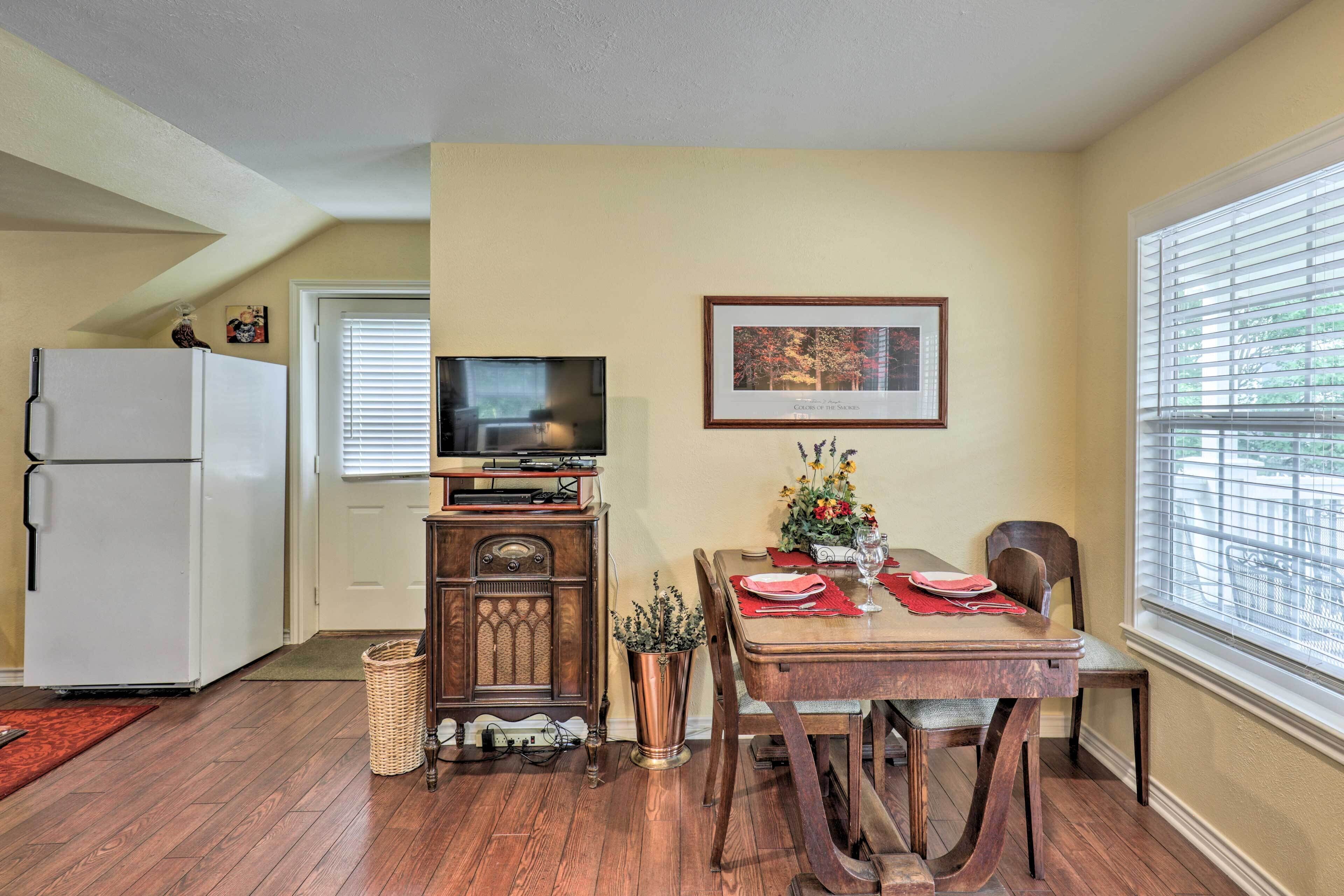 A dining area with a wooden table, chairs, a television, and a refrigerator.