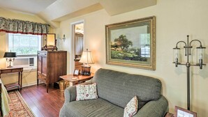 A cozy living room with a sofa, a lamp, a framed painting, and a floor lamp. - Studio in College Station w/ Expansive Deck! (College Station)