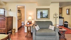 A living room with a sofa, a table with a lamp, a framed picture on the wall, and a view into the kitchen. - Studio in College Station w/ Expansive Deck! (College Station)