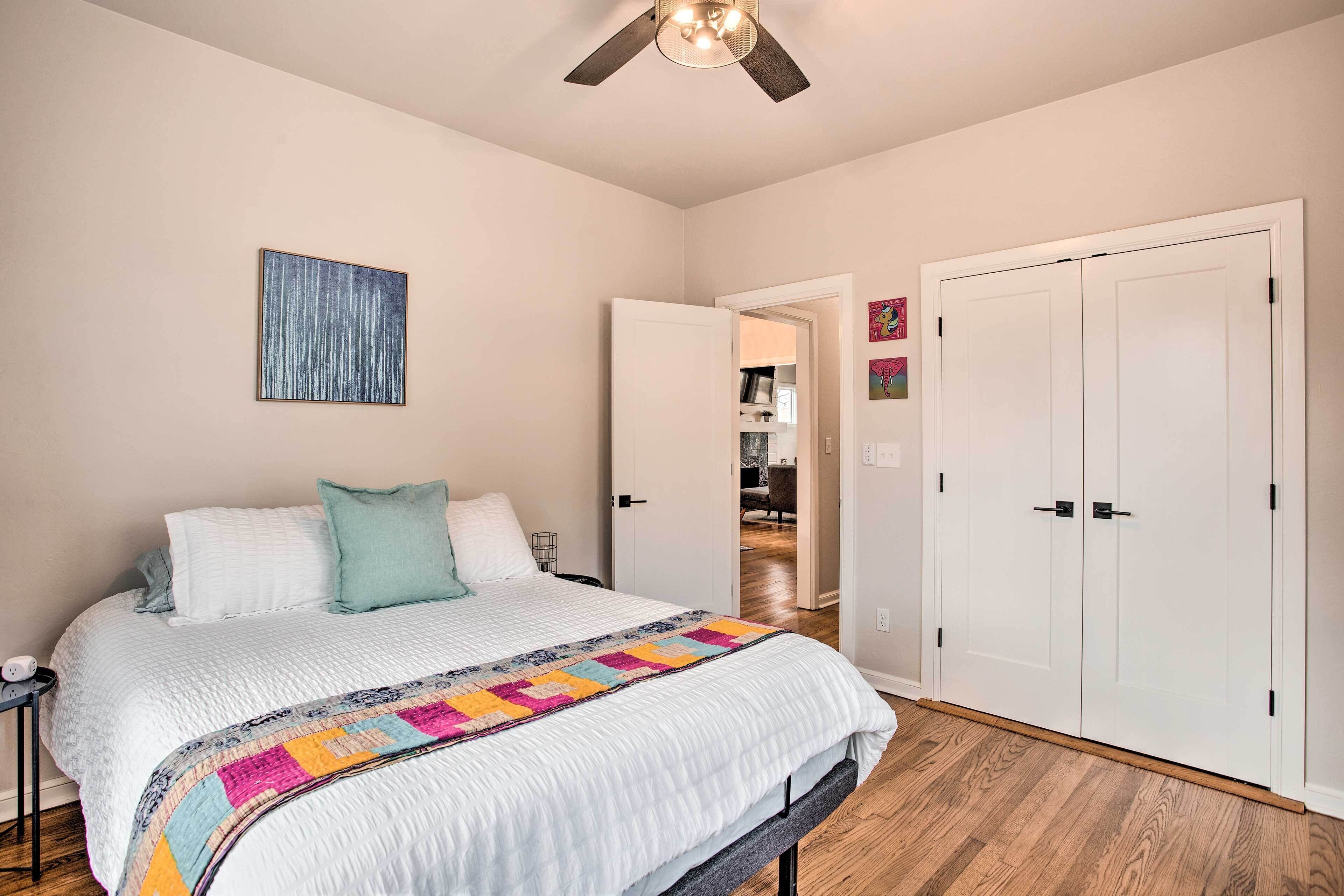 A bedroom with a bed, a ceiling fan, a door, and a hallway.