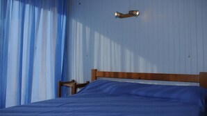 A bedroom with a wooden headboard, a single bed with a blue bedspread, a nightstand, and a wall-mounted light fixture.