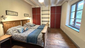 Une chambre à coucher avec un lit en bois, un banc, une fenêtre et des placards intégrés.