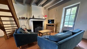 Un salon comprenant un canapé, un fauteuil, une petite table, une cheminée, un téléviseur et une fenêtre donnant sur un paysage verdoyant.