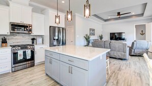 A modern kitchen with white cabinetry, a large island, stainless steel appliances, pendant lighting, and a ceiling fan.