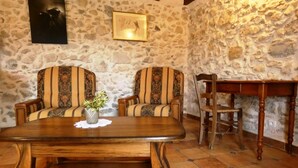 A stone-walled room with two upholstered chairs, a wooden table, and a wooden chair.