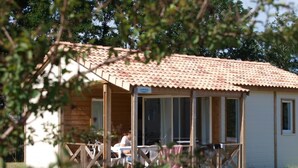 Uma cabana de madeira com telhado de telhas, varanda com grade e uma mesa com cadeiras do lado de fora.