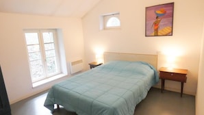 Una camera da letto con un letto, due comodini, una finestra, un termosifone e un quadro appeso al muro.