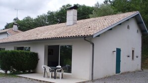 Una casa a un piano con tetto in tegole, una porta d'ingresso e un piccolo patio con due sedie e un tavolo.