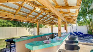 En utomhusbar med en träpergola, en lång bardisk med barstolar och ett läge intill poolen.