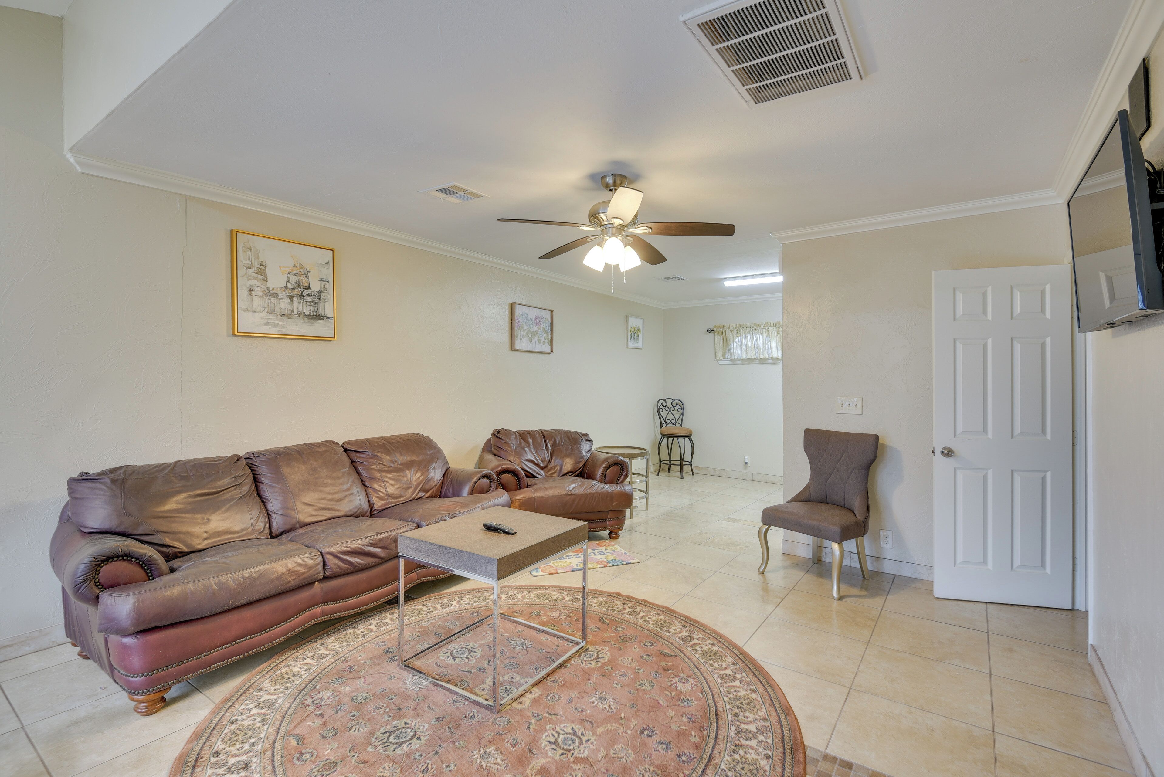 A living room with a brown leather sofa, a coffee table, a patterned rug, a ceiling fan, and a door.