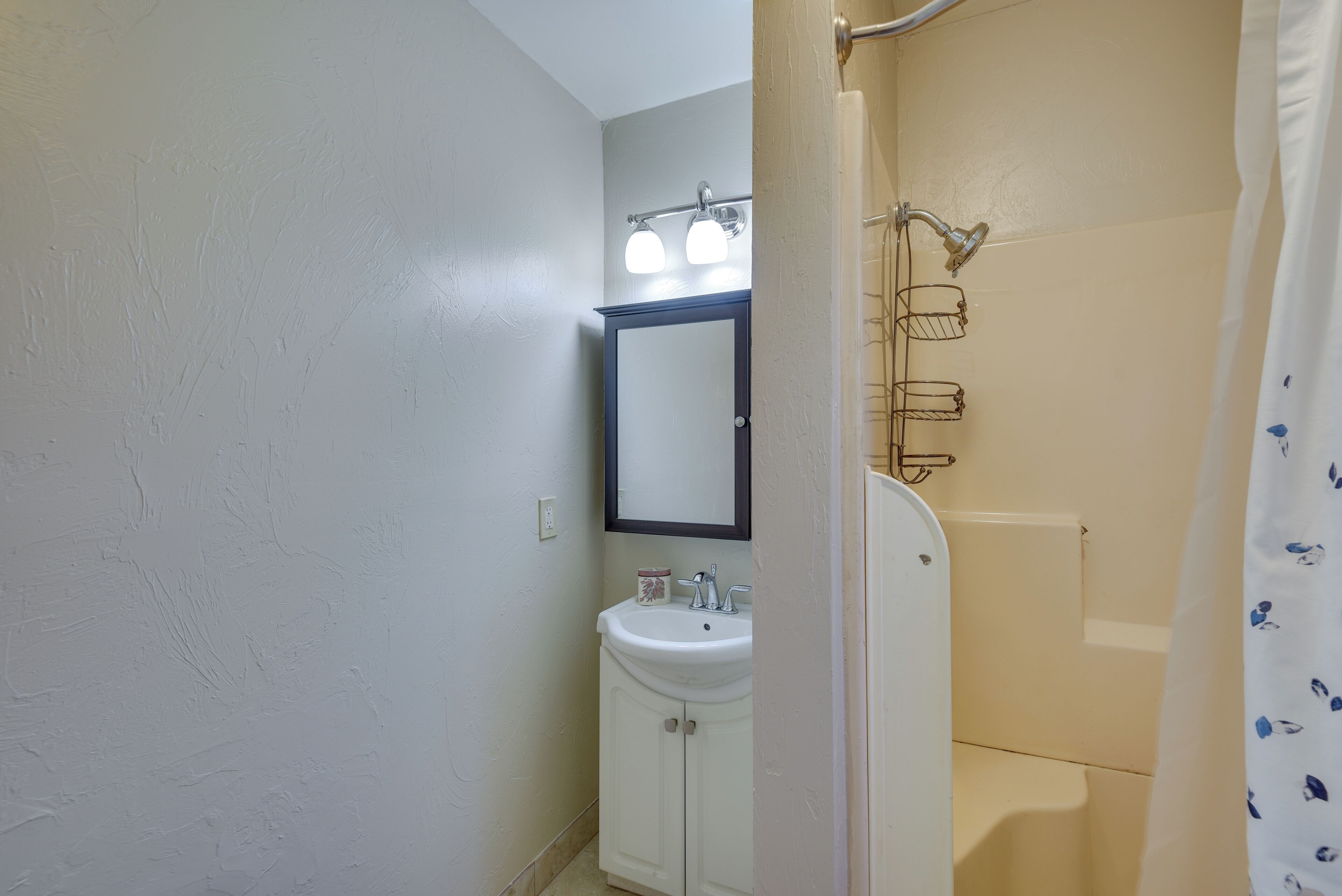 Une salle de bain avec un lavabo blanc, un miroir et une douche avec un rideau de couleur beige.