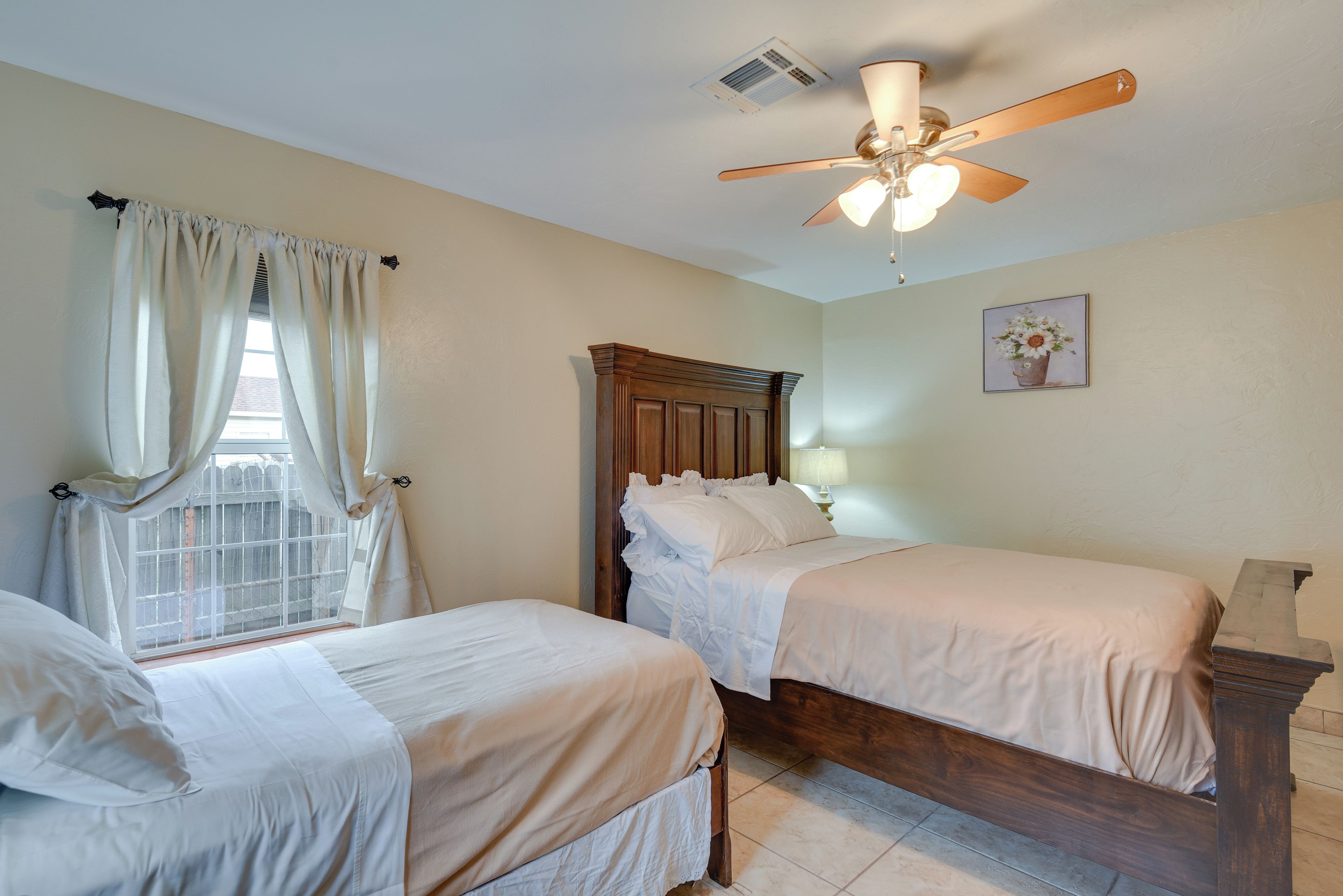 Un dormitorio con dos camas individuales, cabecera de madera, ventilador de techo y una ventana con cortinas.