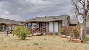 A two-story house with a covered porch, a small garden, and a wooden fence. - Cozy Oklahoma City Home w/ Deck & Gas Grill! (Oklahoma City)