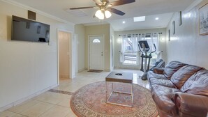 A living room with a ceiling fan, a TV mounted on the wall, a leather sofa, a coffee table, and an exercise bike. - Cozy Oklahoma City Home w/ Deck & Gas Grill! (Oklahoma City)
