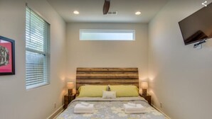 Un dormitorio con cabecera de madera, cama con ropa de cama floral, dos lámparas de noche y un televisor de pantalla plana montado en la pared.