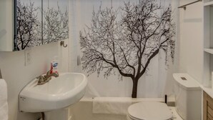 Un baño con lavamanos, inodoro y un adhesivo de árbol en la pared.