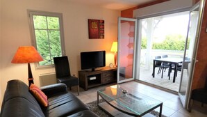 A living room with a sofa, TV, and a glass coffee table. There's a sliding glass door leading to an outdoor patio with a table and chairs. - Chez Detché - Mimizan (MIMIZAN)