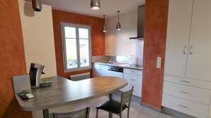A compact kitchen with a dining area, featuring a coffee machine, a window, and a built-in oven. - Chez Detché - Mimizan (MIMIZAN)