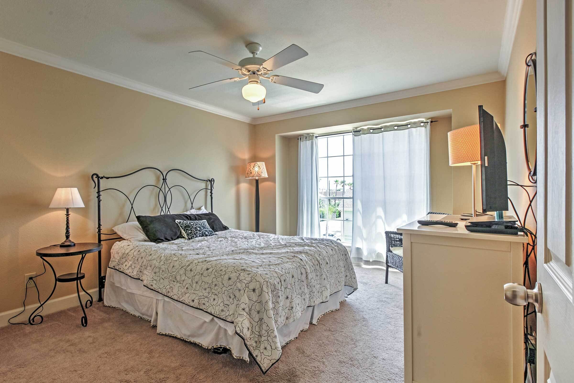 A bedroom with a bed, a ceiling fan, a lamp, a desk with a computer, and a window with curtains.