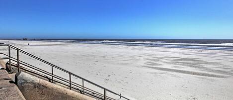 A beach with a concrete walkway and metal railing.