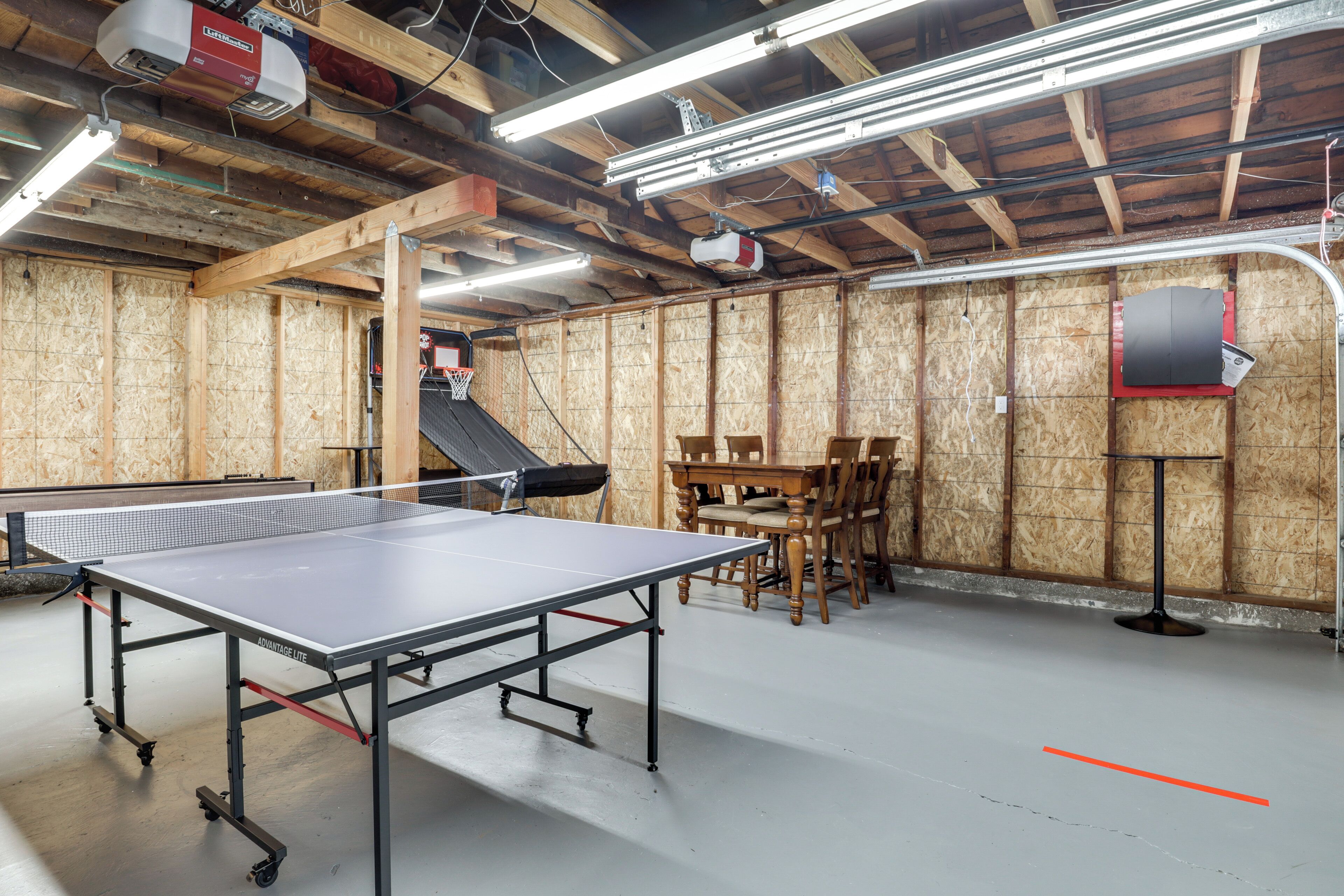 Une table de ping-pong dans une pièce aux murs en bois, avec une table, des chaises et un projecteur fixé au mur.