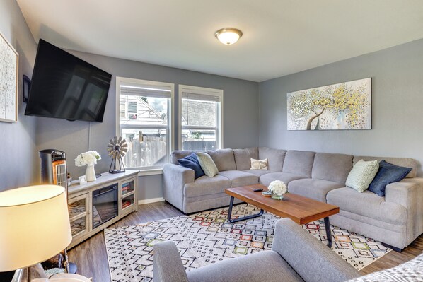 A living room with a grey sofa, a wooden coffee table, a flat-screen TV mounted on the wall, and a decorative painting.