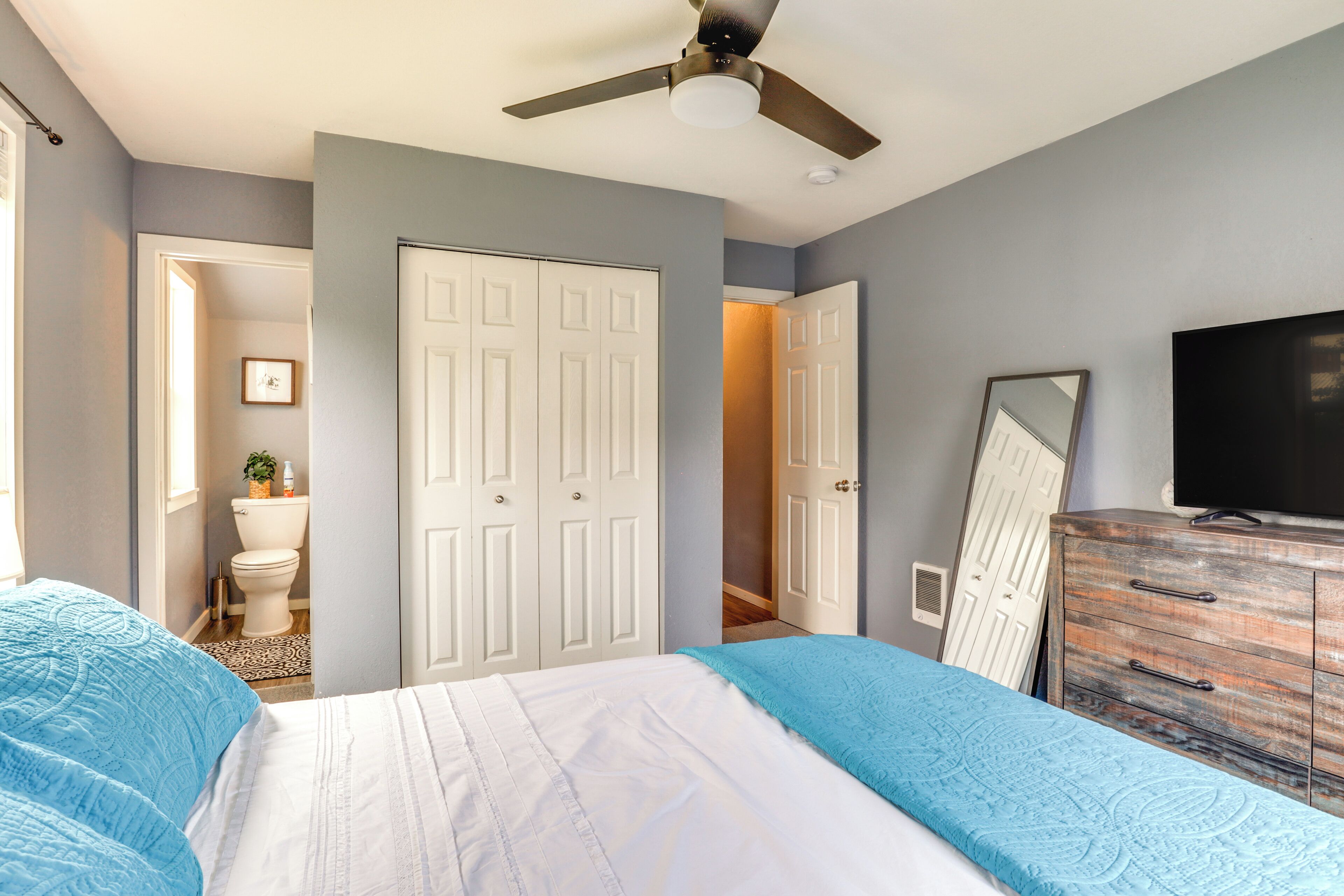 A bedroom with two beds, a ceiling fan, a dresser, and a television.