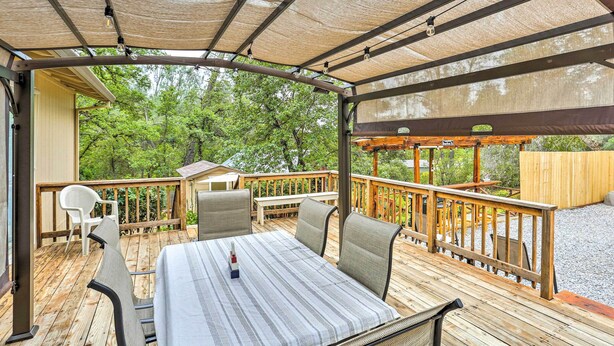 A covered outdoor deck with a table and chairs, surrounded by wooden railings and a view of trees. - Quiet Location! Shasta Lake Home Near Redding (Shasta Lake)