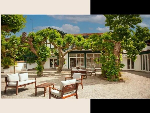 Ein Außenbereich mit Holzkubaturen und Topfpflanzen, im Hintergrund ein Gebäude mit der Aufschrift "HOTEL".