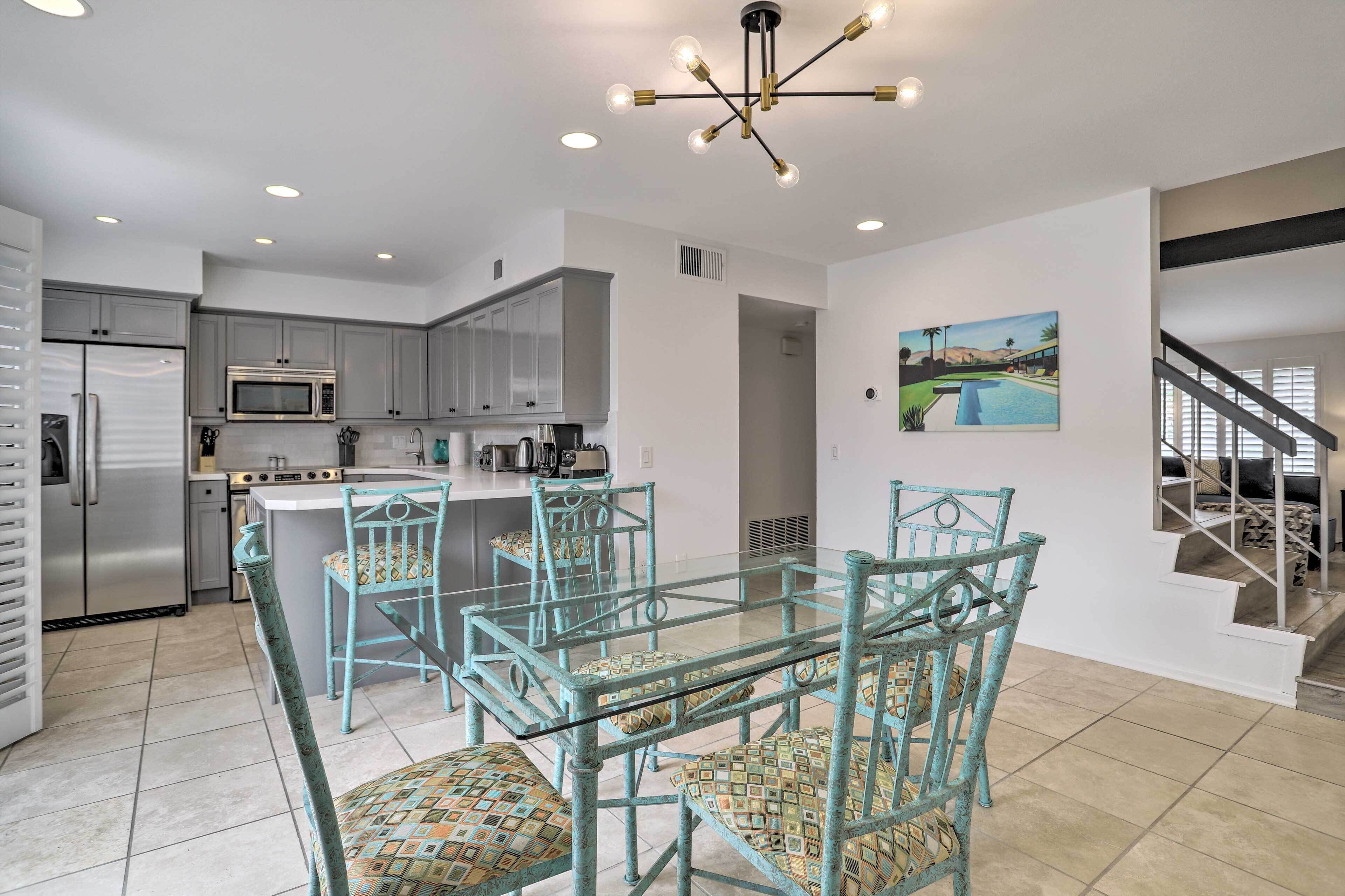 A modern kitchen with stainless steel appliances, a glass dining table, and teal chairs.