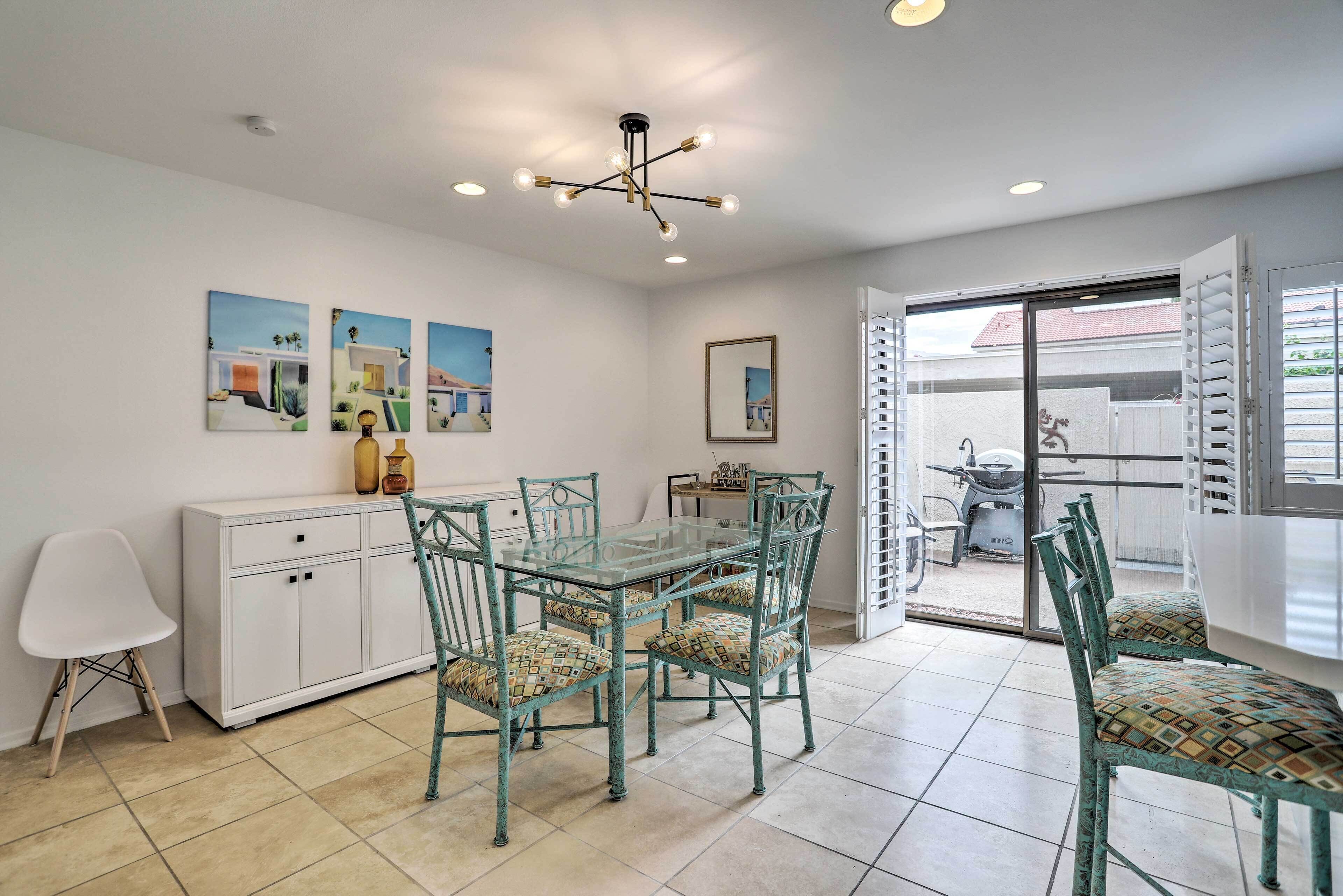 A dining area with a glass table and chairs, a white cabinet, and artwork on the walls.